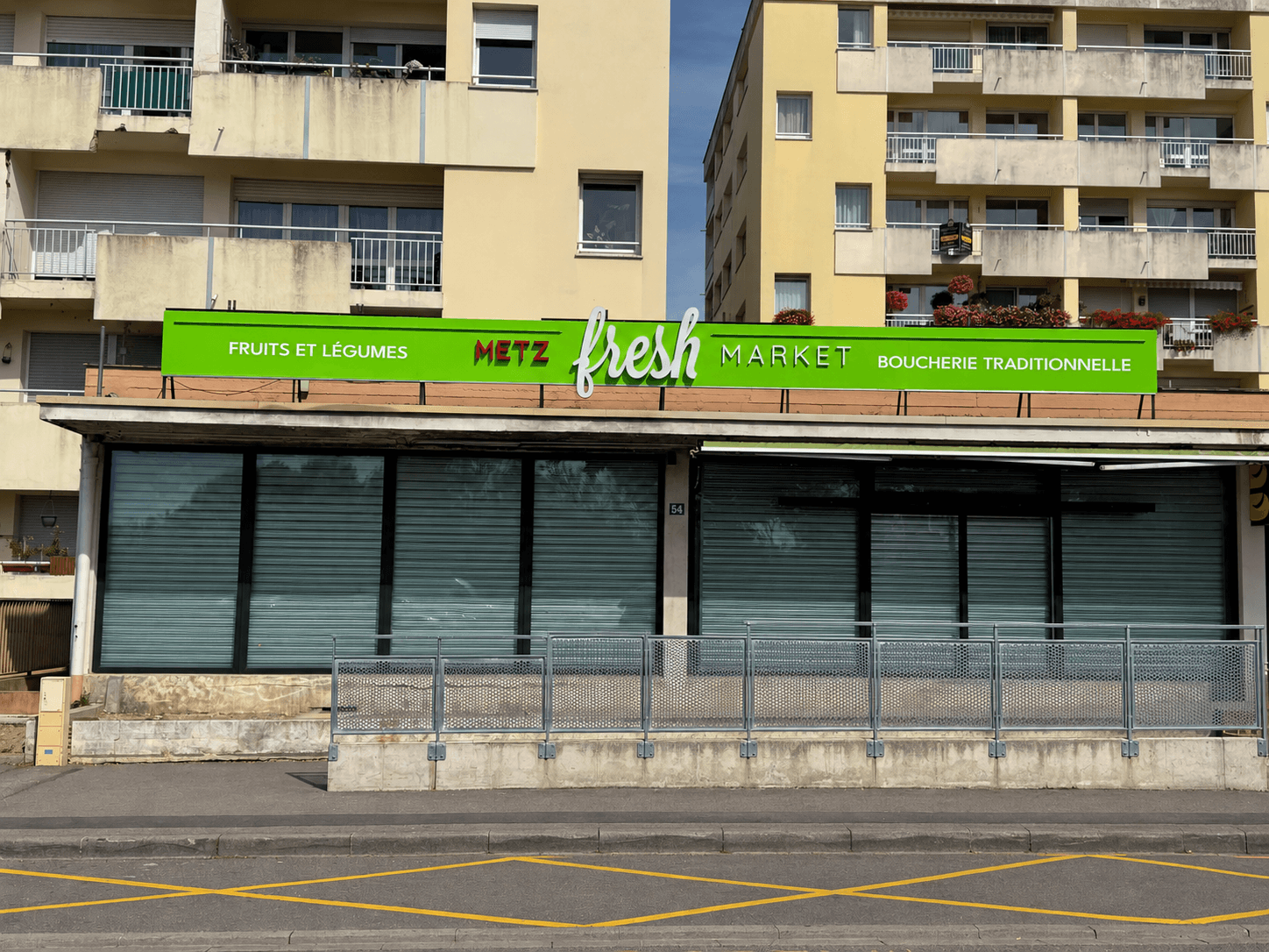Enseigne extérieure Metz Fresh Market remise en état après un incendie, avec nouvelles lettres boîtiers « Metz » sur la façade verte du commerce.