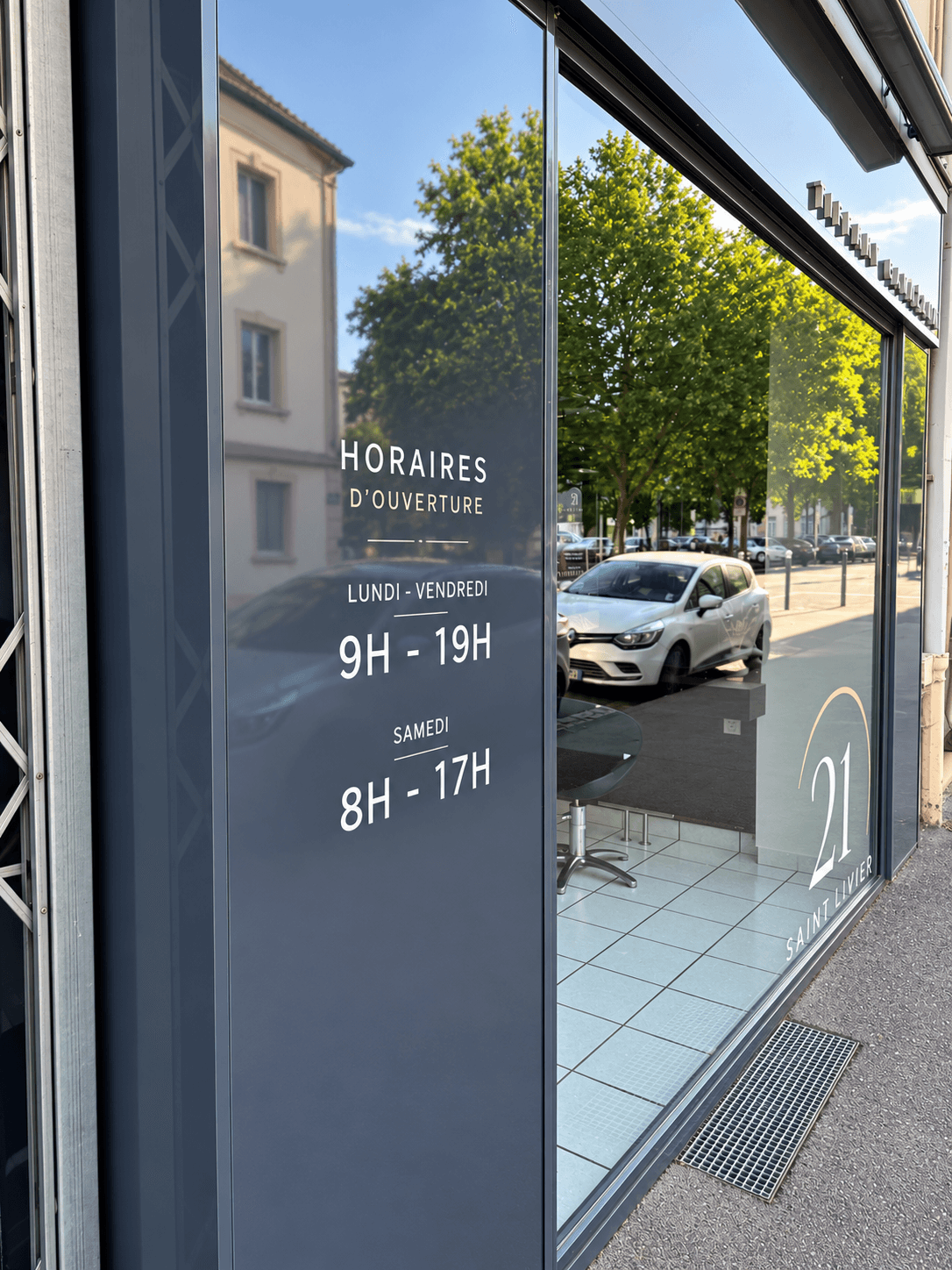 Horaires d’ouverture en adhésif blanc sur la devanture et logo 21 Saint Livier sur la vitrine du salon de coiffure