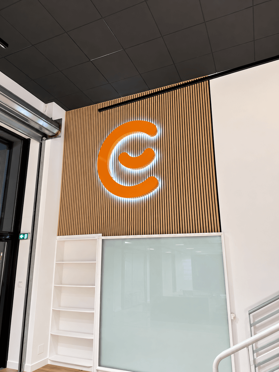 Logo Emma en lettres boîtiers rétro-éclairées posé sur un mur en tasseaux bois dans l’espace intérieur du showroom.