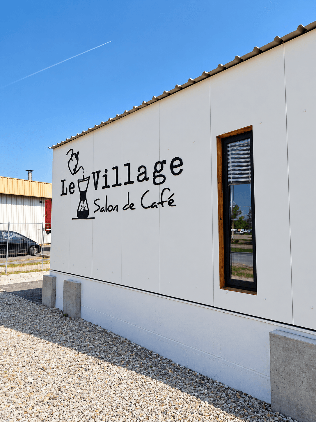 Enseigne extérieure en lettres découpées pour Le Village, salon de café, avec logo et lettrage noir fixés sur la façade du bâtiment.